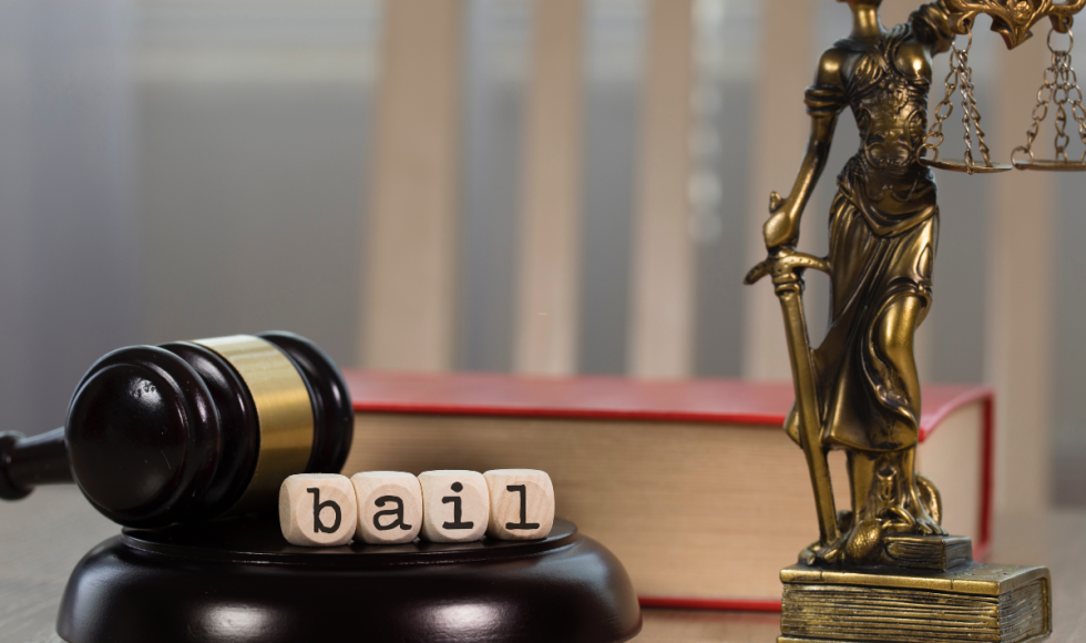 A judge’s gavel rests beside wooden blocks spelling bail with a Lady Justice statue and law book in the background, representing bail bonds in Houston and the benefits of using a bail bond for quick release and legal support.