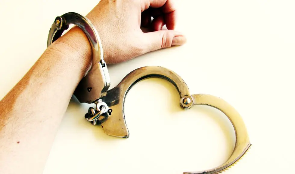 A person’s wrist secured in metal handcuffs against a light background, symbolizing being out on bail in Houston and the serious consequences of violating bail conditions or making mistakes while awaiting court.
