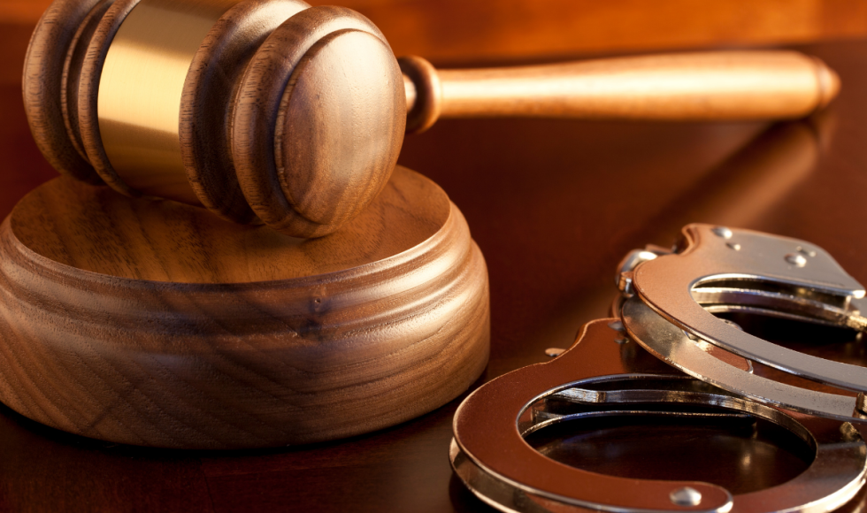 A wooden judge’s gavel rests on its sound block beside a pair of metal handcuffs on a polished desk. The image symbolizes the intersection of court decisions and criminal custody, visually reinforcing the legal process surrounding appeal bonds and a defendant’s potential release while a case is under review in Houston.