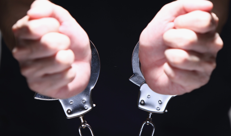 A person’s wrists are secured in metal handcuffs, with both hands held forward against a dark background. The image represents an arrest or detention, visually reinforcing the serious criminal nature of aggravated assault charges and the legal process surrounding bond and release in Houston.