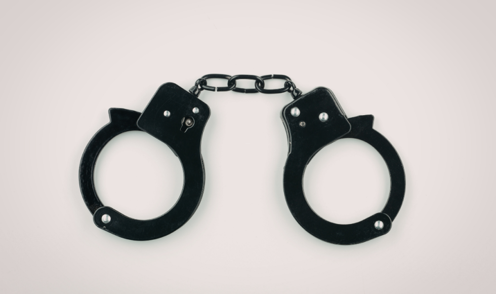 A pair of black metal handcuffs lies centered against a plain, light background, linked by a short chain. The stark, minimal composition emphasizes restraint and custody, visually representing the serious consequences that can follow a bond violation or new criminal charge while out on bond in Houston.