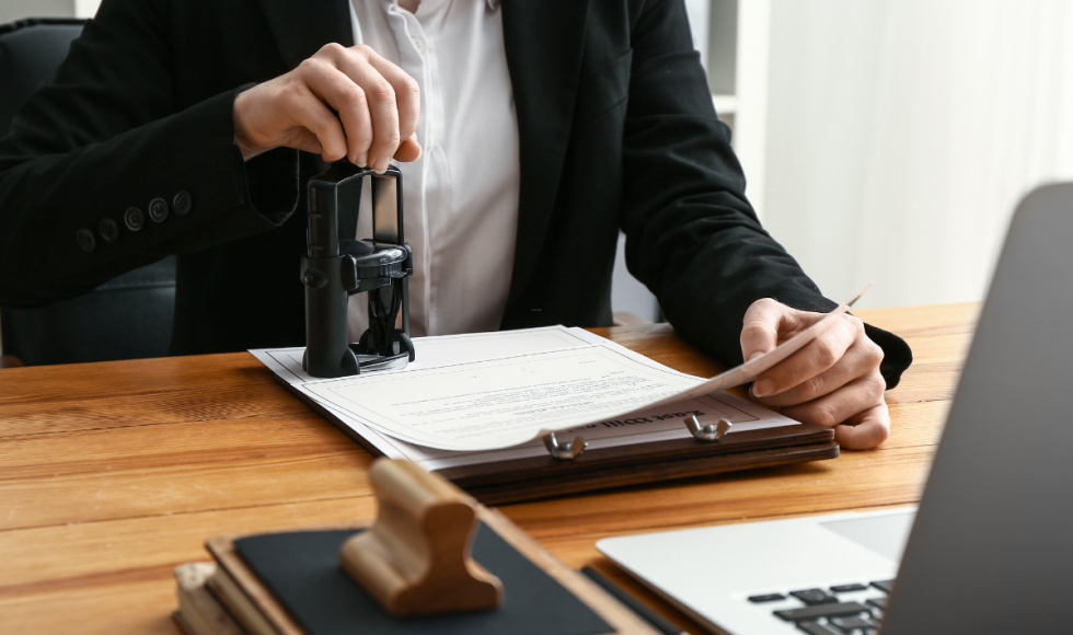 Person notarizing a legal document with an official notary stamp beside a laptop, illustrating state-authorized public notary services for legal documents in Houston.