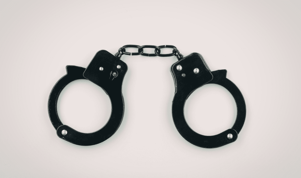 A pair of black metal handcuffs lies centered against a plain, light background, linked by a short chain. The stark, minimal composition emphasizes restraint and custody, visually representing the serious consequences that can follow a bond violation or new criminal charge while out on bond in Houston.
