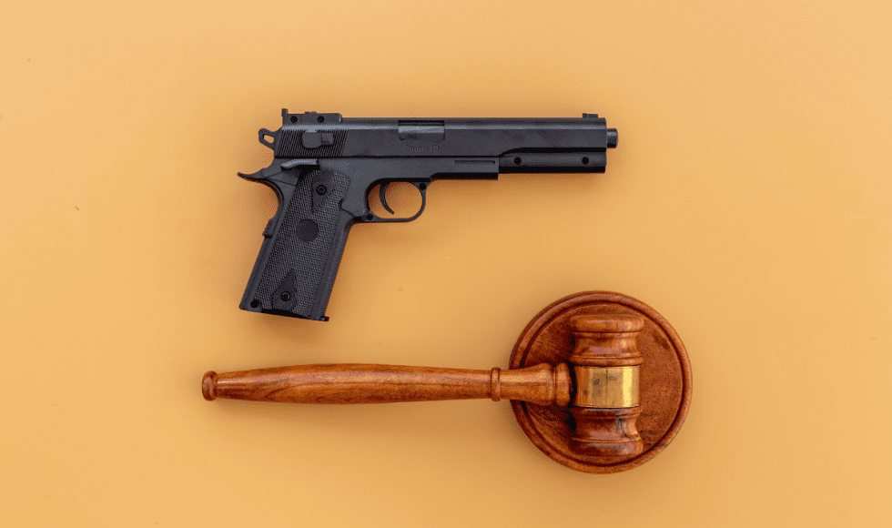 Handgun placed above a wooden judge’s gavel on a neutral background, symbolizing the intersection of firearm laws and the legal system in criminal cases.
