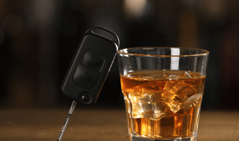 Car keys positioned beside a glass of whiskey on a table, symbolizing drunk driving and the legal consequences associated with DUI offenses.