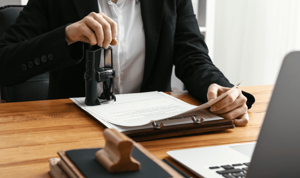 Person notarizing a legal document with an official notary stamp beside a laptop, illustrating state-authorized public notary services for legal documents in Houston.